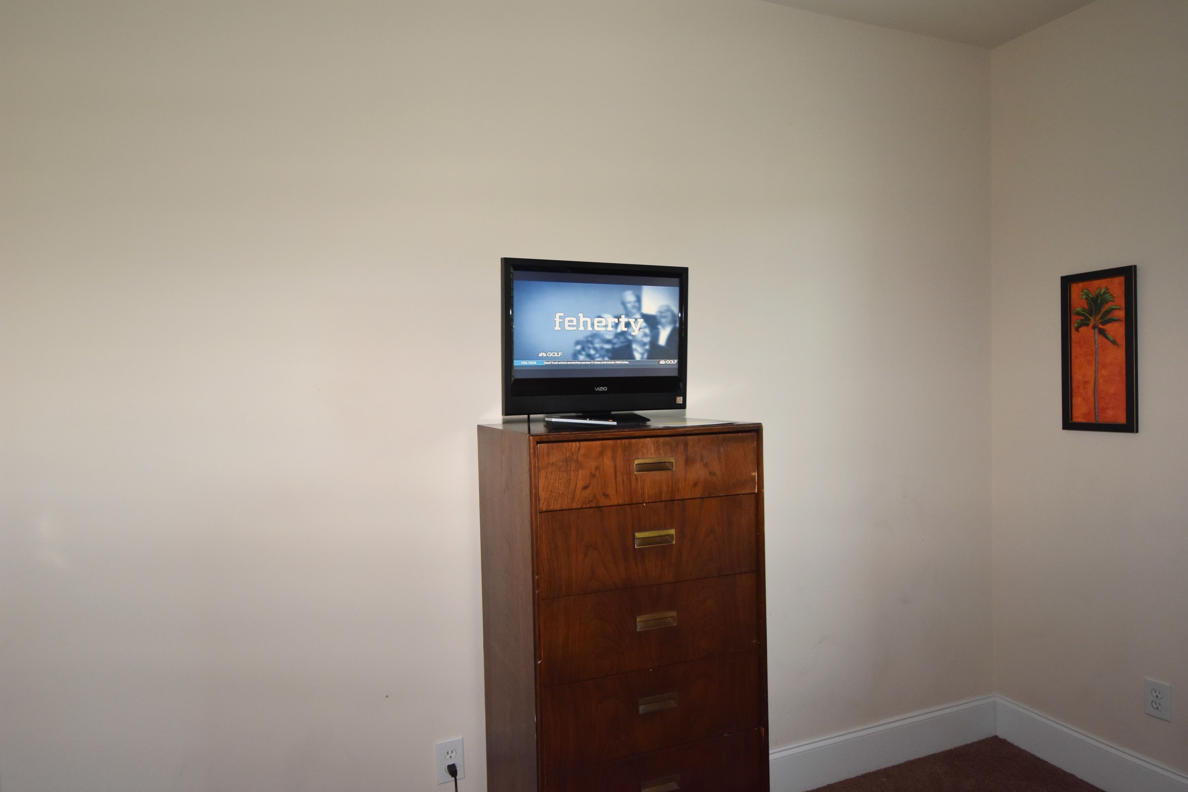 A television on a wooden cabinet in a room with plain walls and a framed picture.