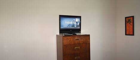 A television on a wooden cabinet in a room with plain walls and a framed picture.