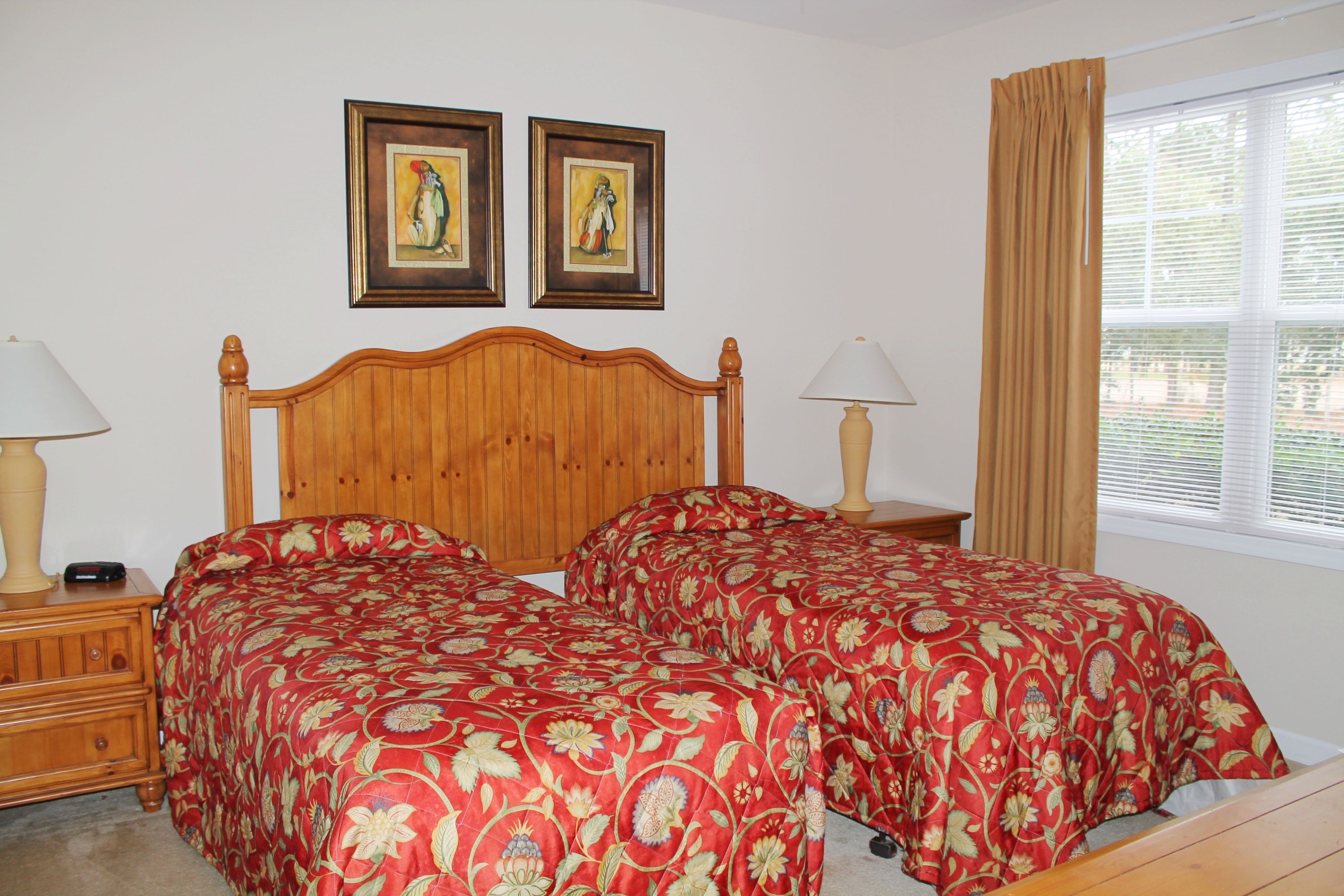 A double bed with floral bedding, wooden headboard, bedside tables with lamps, and two framed pictures on the wall.