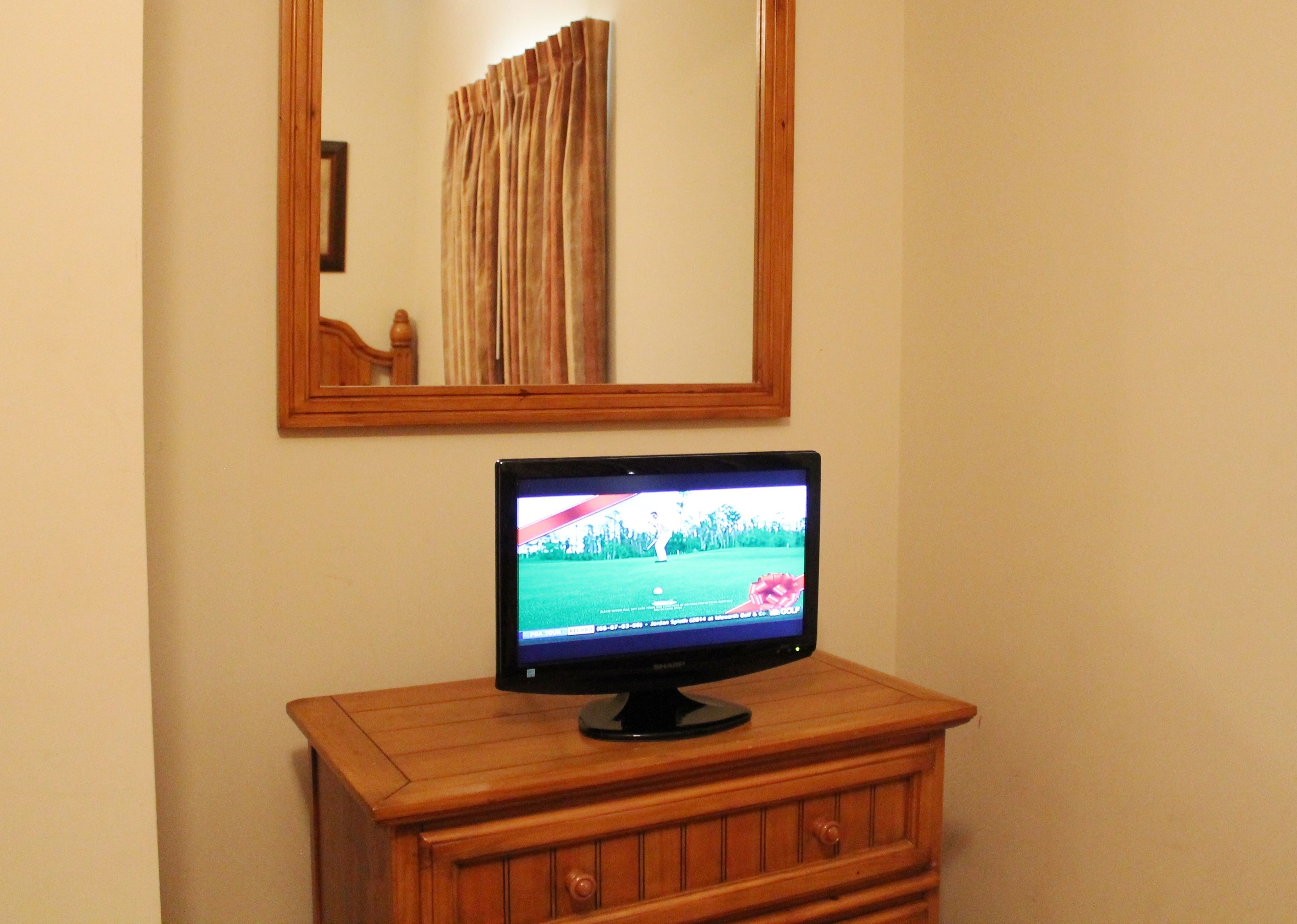 A television on a wooden dresser in a room with a mirror above it.
