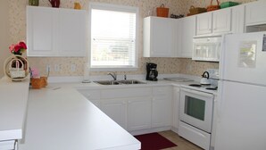 A kitchen with white cabinets, a stove, a microwave, and a refrigerator. There is a window with blinds, a sink, and a red rug on the floor. - 614 Willow Bend (North Myrtle Beach)