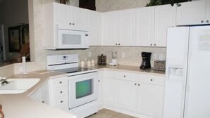 A kitchen with white cabinets, a microwave, a stove, a refrigerator, and a coffee maker. - 734 The Havens (North Myrtle Beach)
