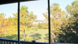 A view from a window overlooking a grassy area with trees and a building in the distance. - 734 The Havens (North Myrtle Beach)