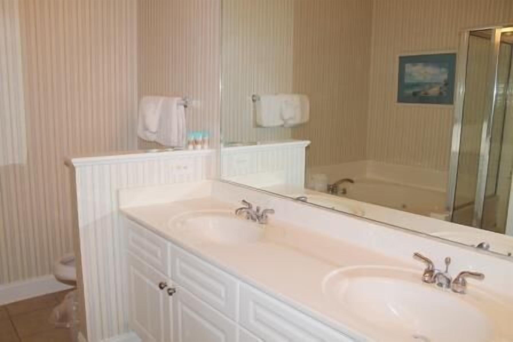 A bathroom with a double sink vanity, a large mirror, and a shower area.