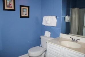 A bathroom with blue walls, a white toilet, a sink with a mirror, and two framed pictures on the wall. - 734 The Havens (North Myrtle Beach)