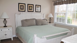 A neatly arranged bedroom with a white bed, two bedside tables, and a window with blinds.