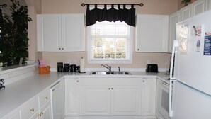A kitchen with white cabinets, a black window valance, a sink, a stove, and a refrigerator.