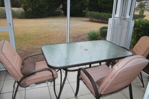 A glass-top table with four chairs, a tiled floor, and a view of a grassy area through a glass door. - 614 Ironwood (North Myrtle Beach)