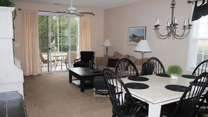 A dining area with a white table, black chairs, a chandelier, and a view through a glass door to an outdoor patio.