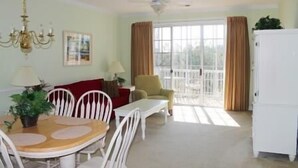 A living room with a dining table, chairs, a sofa, a chair, a lamp, a ceiling fan, and a window with curtains. - 1321 The Havens (North Myrtle Beach)