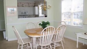 A dining area with a round table and white chairs, a chandelier, and a window with blinds. - 1321 The Havens (North Myrtle Beach)