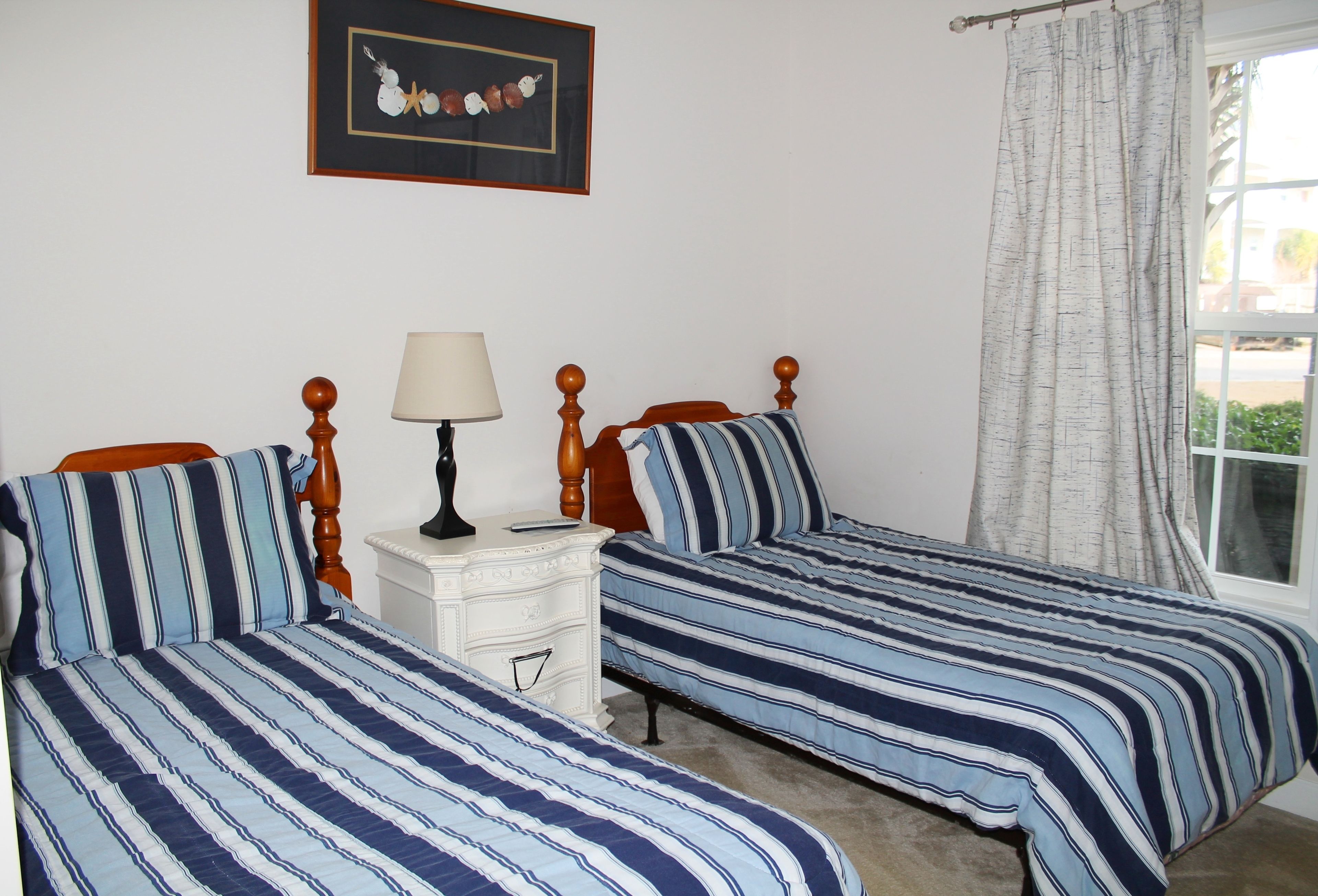 A bedroom with two beds, a bedside table with a lamp, and a framed picture on the wall.