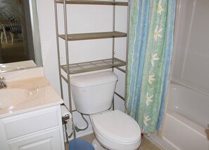 A bathroom with a toilet, a sink, and a metal shelving unit. - 1212 The Havens (North Myrtle Beach)