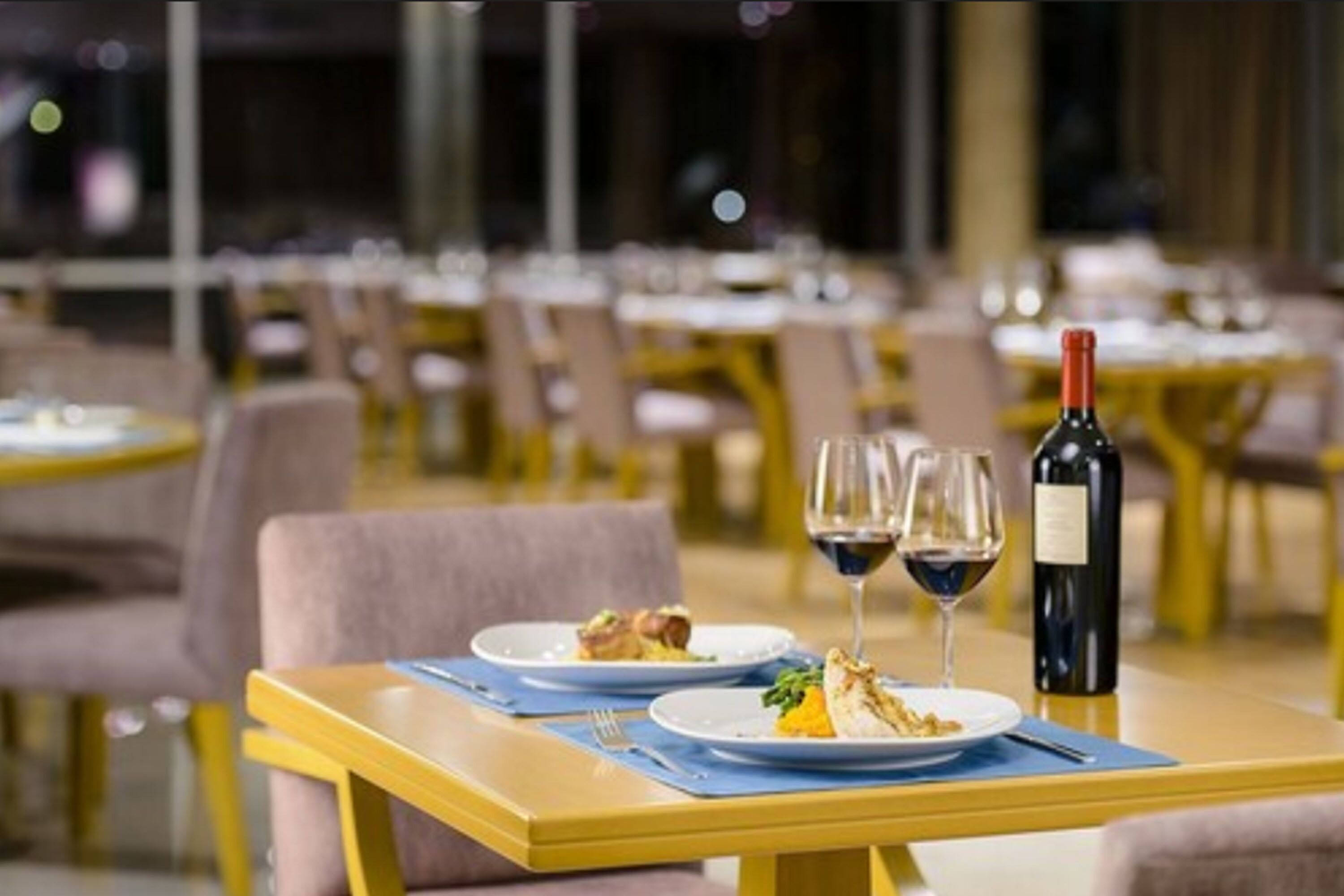 Una mesa de comedor con dos platos de comida, dos copas de vino y una botella.