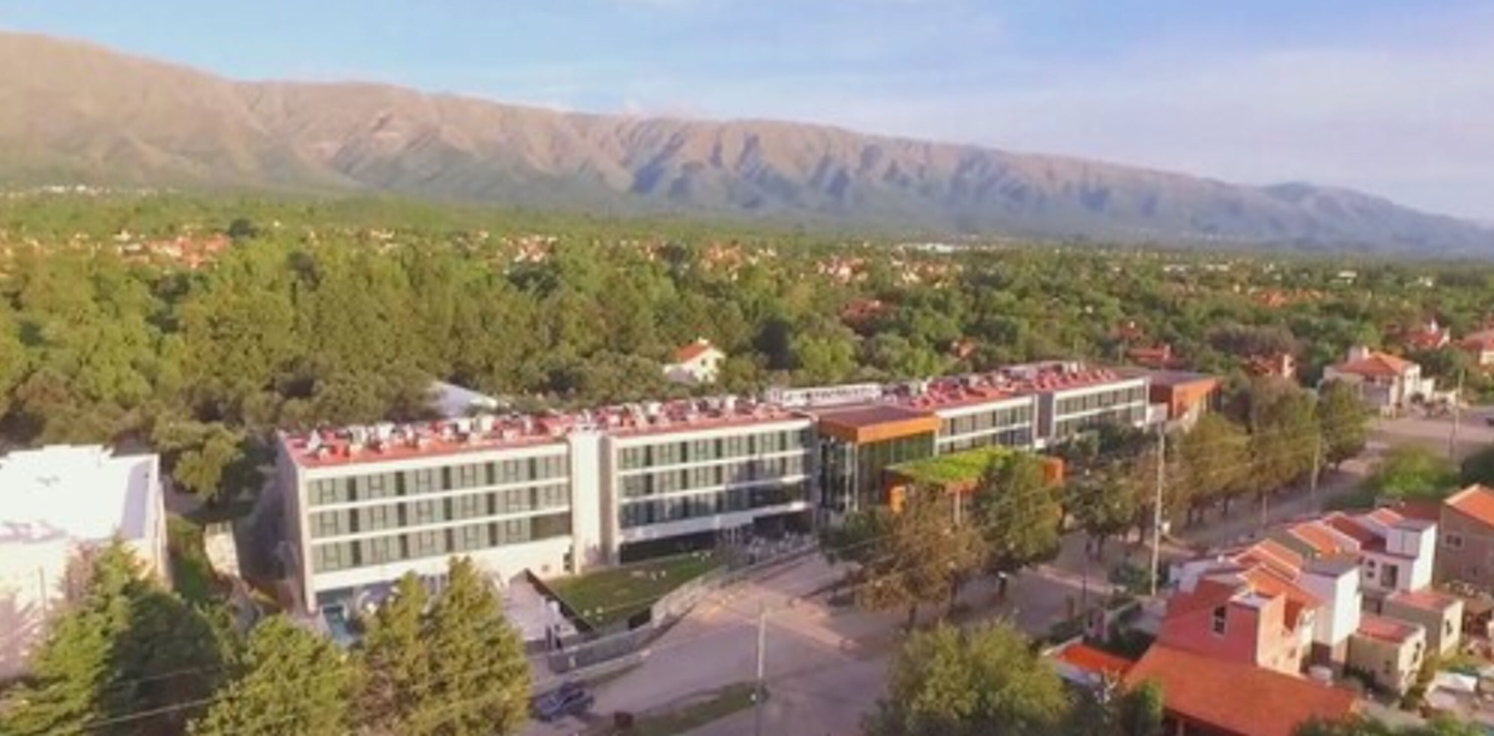 A modern building with multiple floors, surrounded by trees and residential buildings.