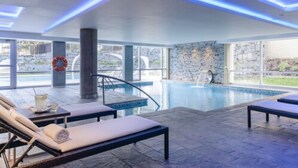 An indoor swimming pool with lounge chairs and a stone wall. - Epic Hotel Villa de Merlo (Merlo)