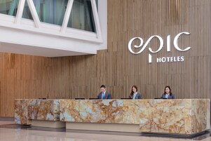 Mostrador de recepción en Epic Hotels con diseño de mármol, un panel de pared de madera y un amplio ventanal arriba.