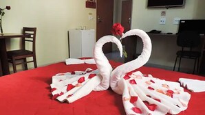 Un lit recouvert d’une couverture rouge, un mur blanc, une porte, un bureau, une chaise et un téléviseur fixé au mur.