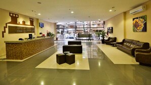 Un vestíbulo de hotel con mostrador de recepción, zona de estar y un amplio ventanal con vistas a la ciudad.