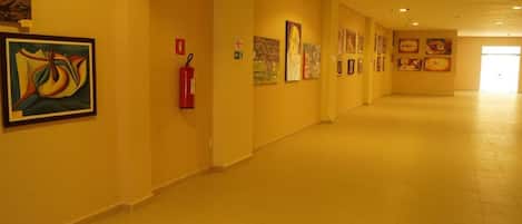Un pasillo con obras de arte en las paredes, un extintor y una puerta al final.