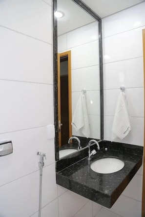 Une salle de bain avec un lavabo à vasque et un plan de toilette noir, un miroir et une douchette à main.