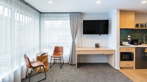 A modern kitchen with a flat-screen TV, wooden cabinets, and a built-in microwave. - Takapuna International Motor Lodge (Auckland)