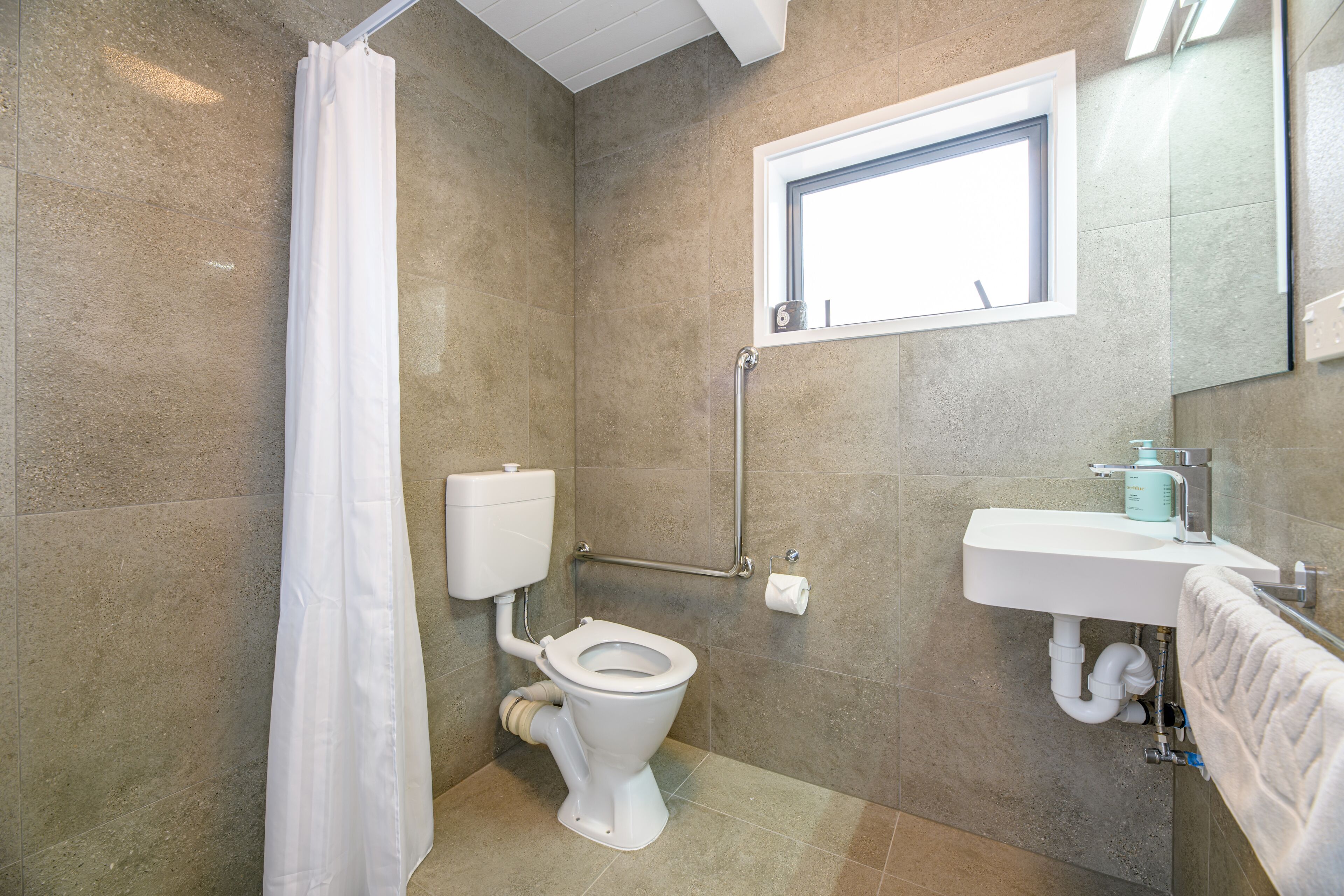 A bathroom with a toilet, shower curtain, sink, and window.