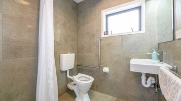 A bathroom with a toilet, shower curtain, sink, and window.