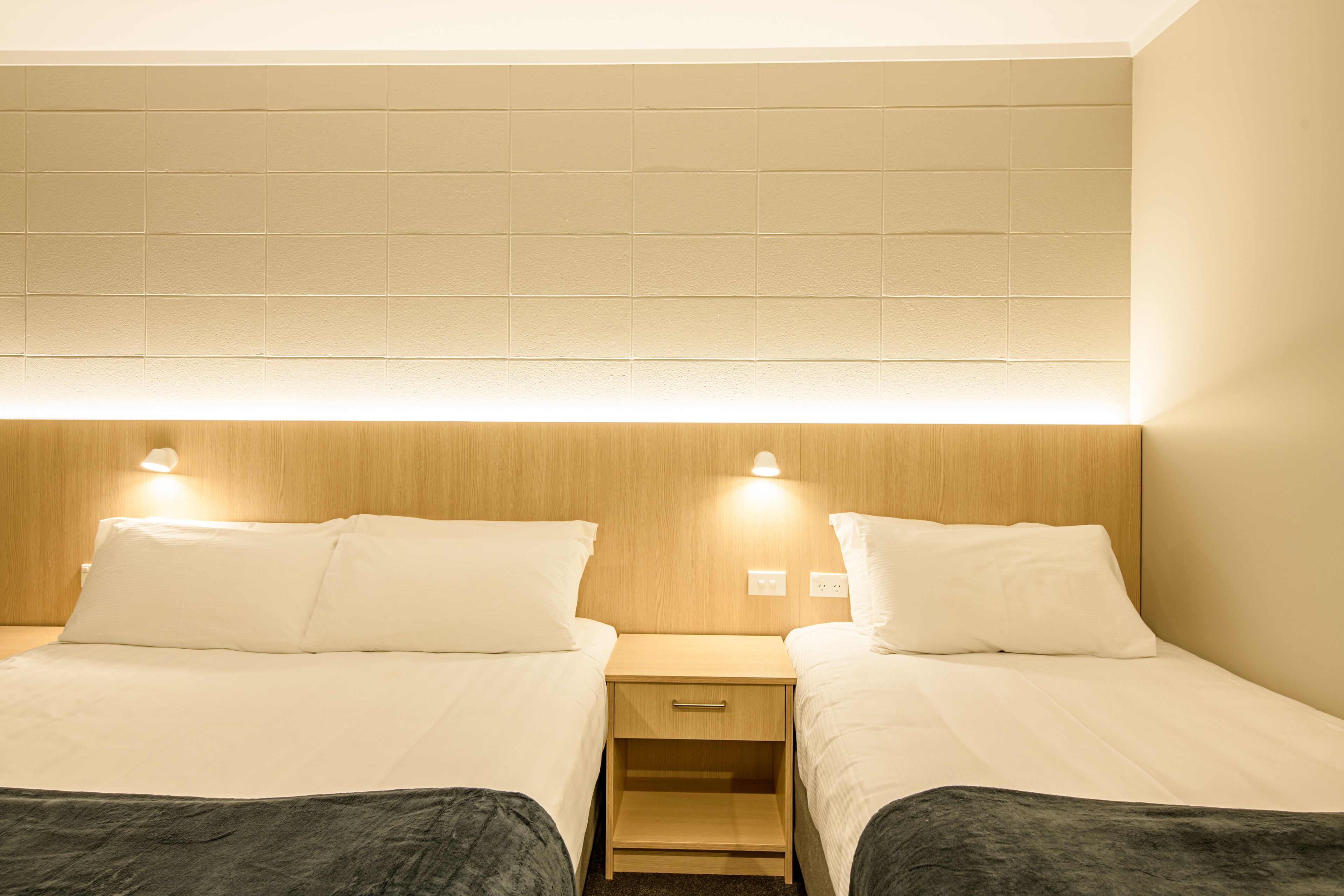 Une chambre d’hôtel avec deux lits, une tête de lit en bois, des tables de chevet avec des lampes et un petit tiroir.