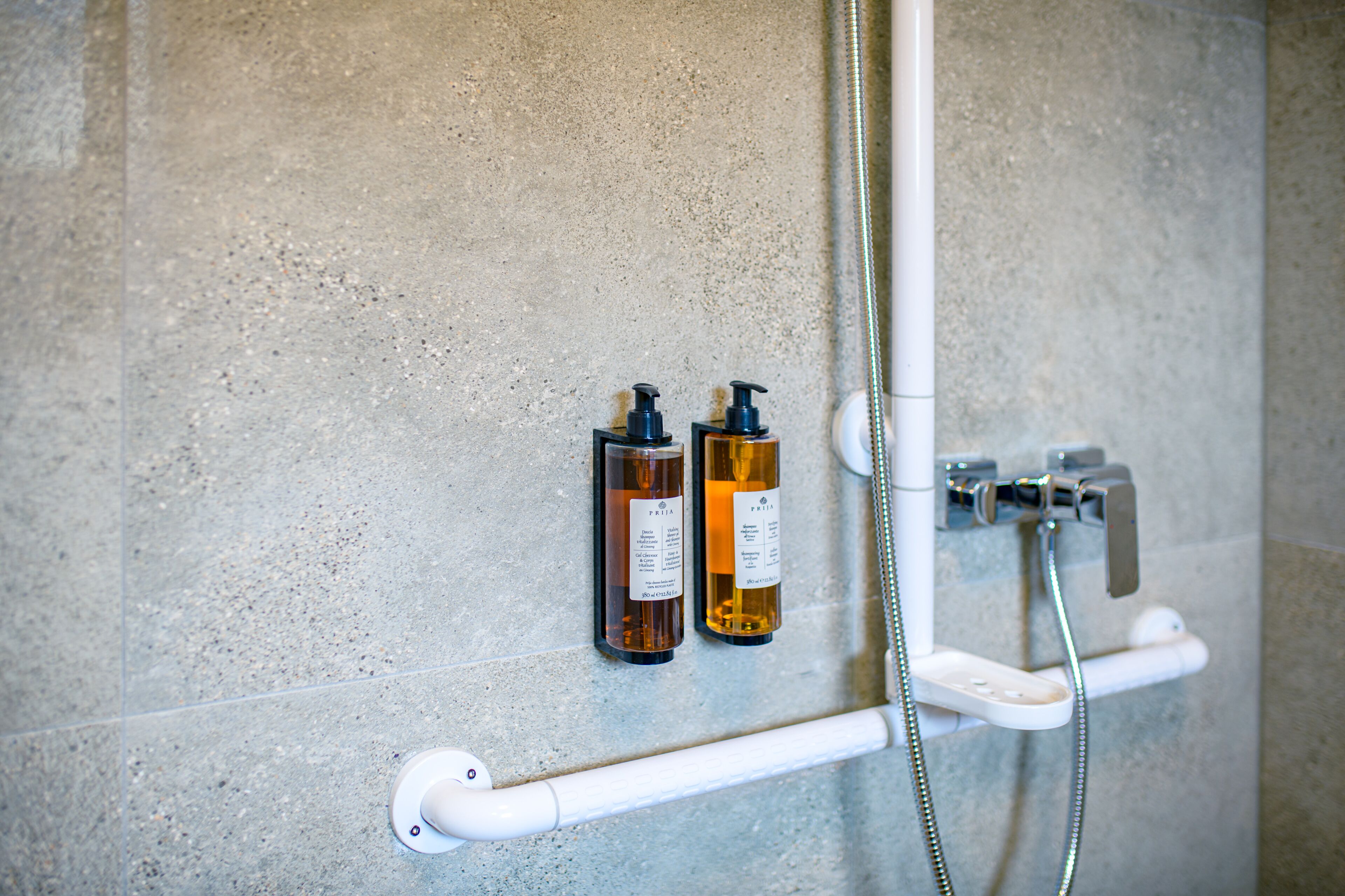 A shower area with a handheld showerhead, a handheld soap dispenser, and a soap bottle.