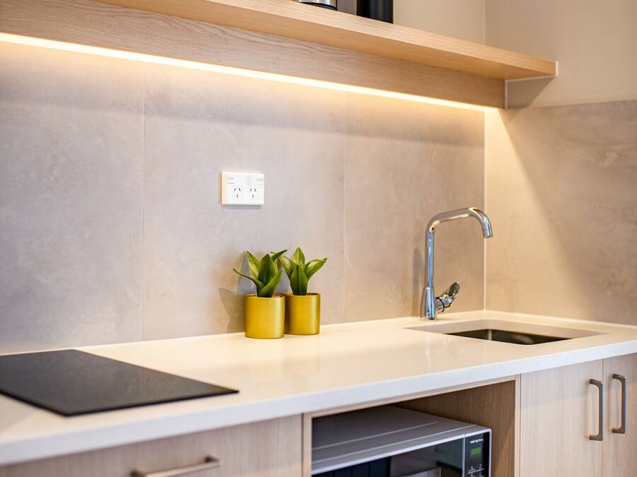 A modern kitchen with a built-in microwave, a stainless steel toaster, and a sink. There are two potted plants on the countertop.