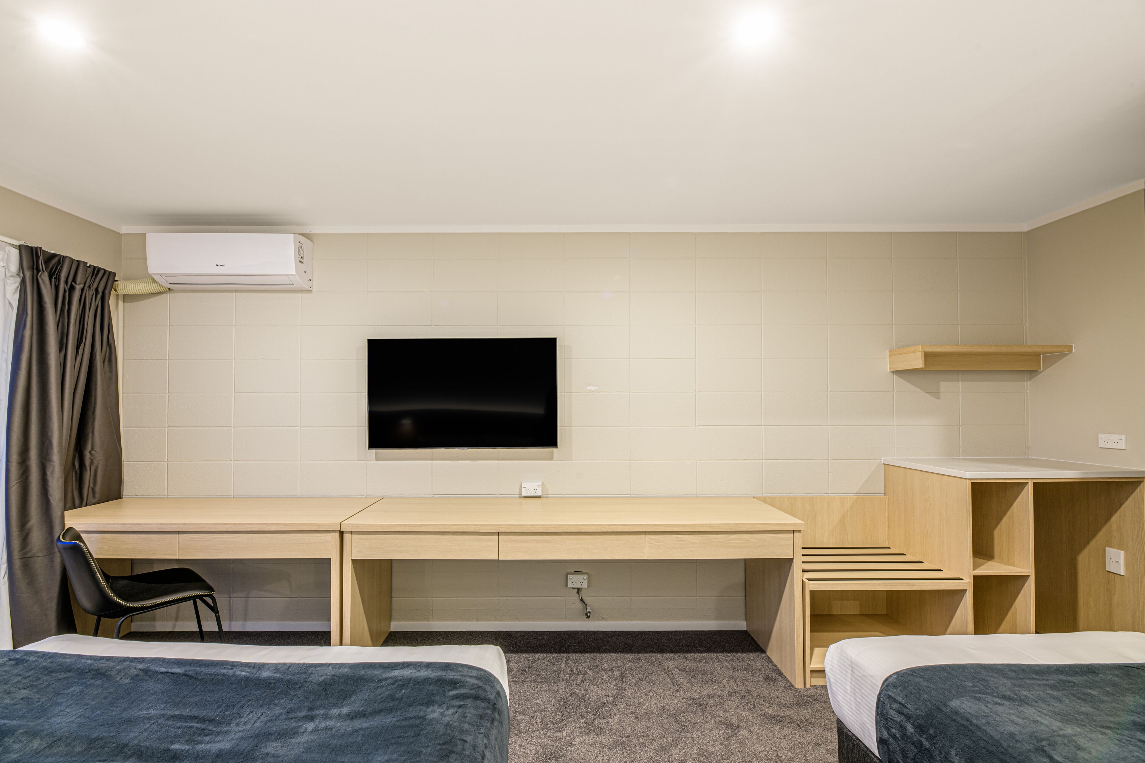 Quarto de hotel com cama, escrivaninha, cadeira, televisão e guarda-roupa.
