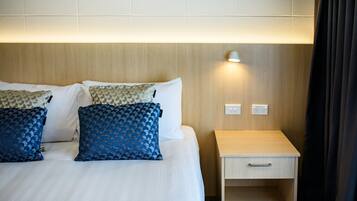 A hotel room with a neatly made bed, two pillows, a bedside table with a lamp, and a power outlet.
