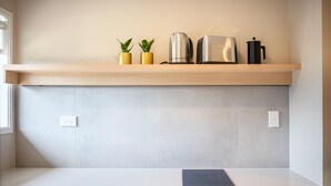 A kitchen with a wooden countertop, a white backsplash, and a shelf with two potted plants and kitchen appliances. - Takapuna International Motor Lodge (Auckland)
