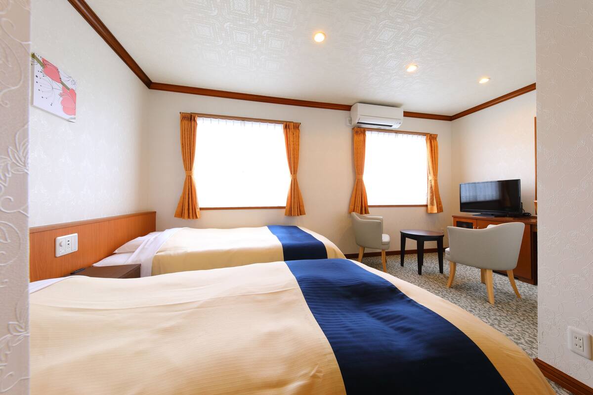 A hotel room with two beds, a desk, a chair, and a television.