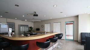 A modern bar area with a curved counter, black bar stools, a projector on the ceiling, and a clock on the wall. - Business Hotel Star (Beppu)