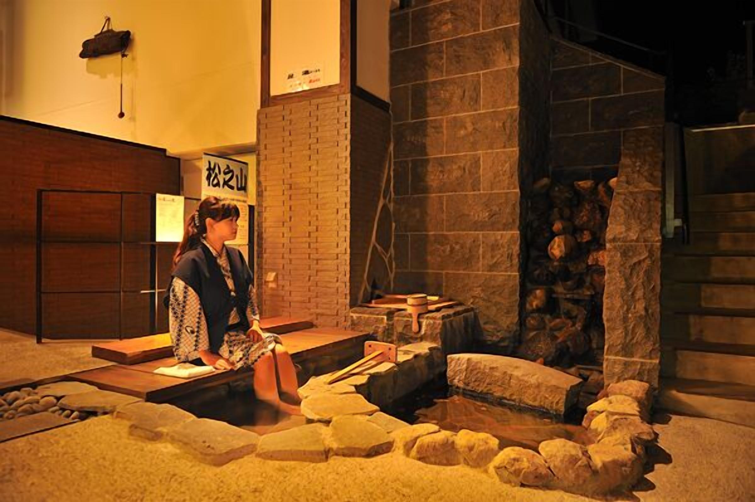Un onsen japonais traditionnel, avec un bain en pierre, des marches en bois et une pancarte en japonais.
