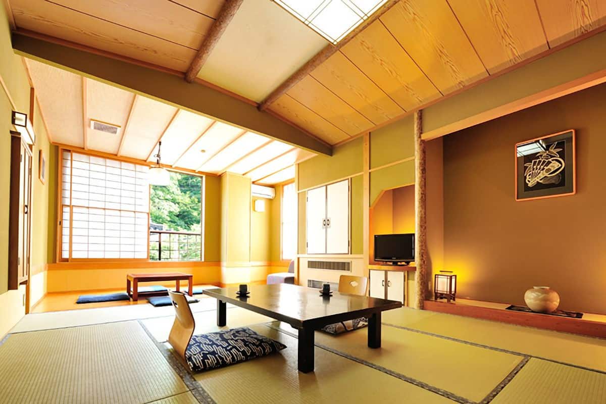 A traditional Japanese room with tatami flooring, a low table, cushions, a television, and a decorative vase.