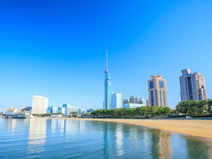 A coastal cityscape with a prominent skyscraper, a sandy beach, and a clear blue sky.