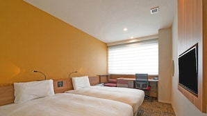 Ein Hotelzimmer mit zwei Betten, einem Schreibtisch mit Stuhl, einem Fernseher und einem Fenster mit Jalousien.