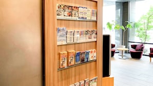 Ein Empfangsbereich mit einer Holzauslage, die verschiedene Broschüren und Zeitschriften präsentiert. Zwei Sitzbereiche mit modernen Stühlen und einem kleinen Tisch laden zum Verweilen ein.