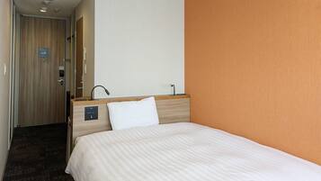Une chambre d’hôtel avec un lit, une tête de lit en bois, une petite table de chevet, un miroir et une porte donnant sur un couloir.
