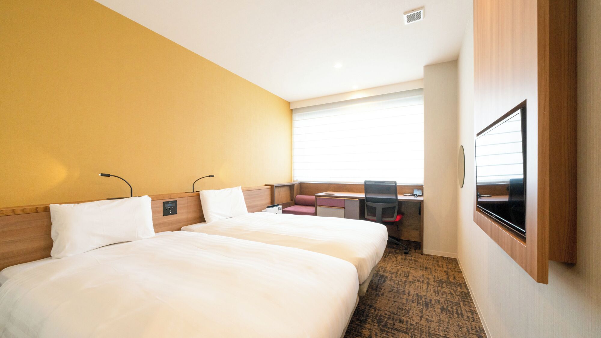 A hotel room with two beds, a desk, a chair, a television, and a window with blinds.
