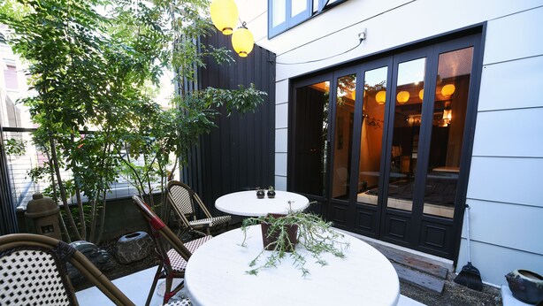 A patio with a round table and chairs, a potted plant, and a broom leaning against the wall. - Kyobijin (Kyoto)