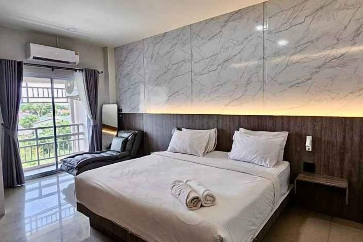 A hotel room with a large bed, a marble wall, a balcony, and a view of greenery.