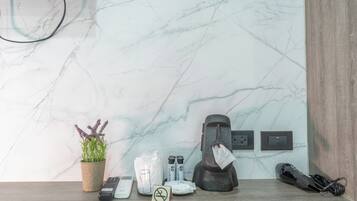 A bathroom with a marble wall, a potted plant, a towel dispenser, a trash bin, and a hairdryer on the floor.