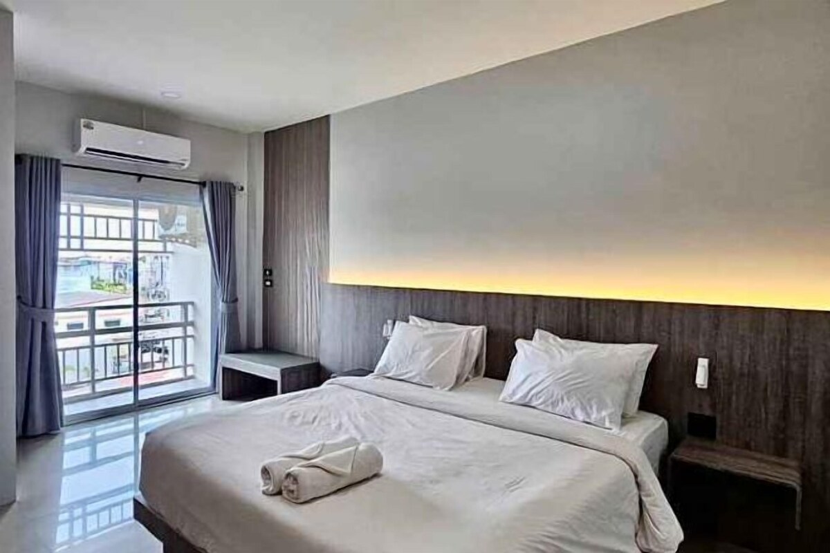 A hotel room with a large bed, a bedside table, a nightstand, and a view of the outside.