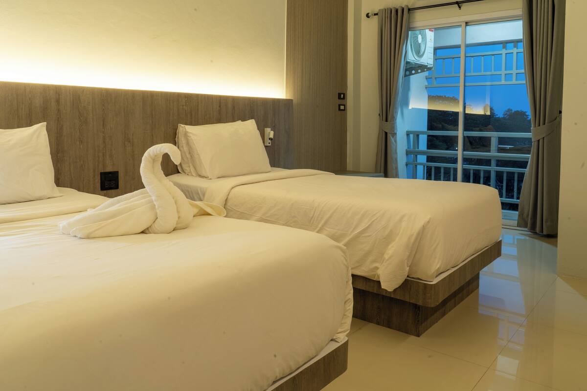 A hotel room with two beds, a large window with curtains, and a ceiling fan.