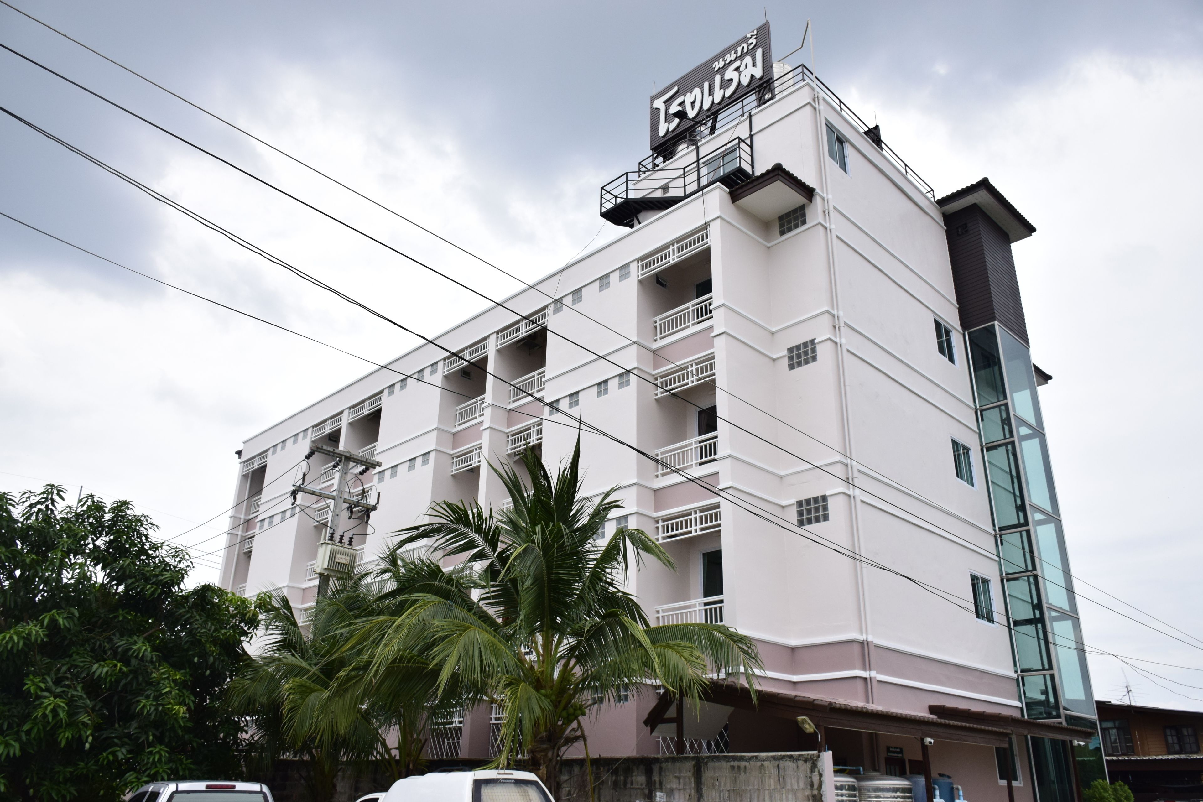 A multi-story building with balconies, a sign in a foreign language, and a palm tree in front.