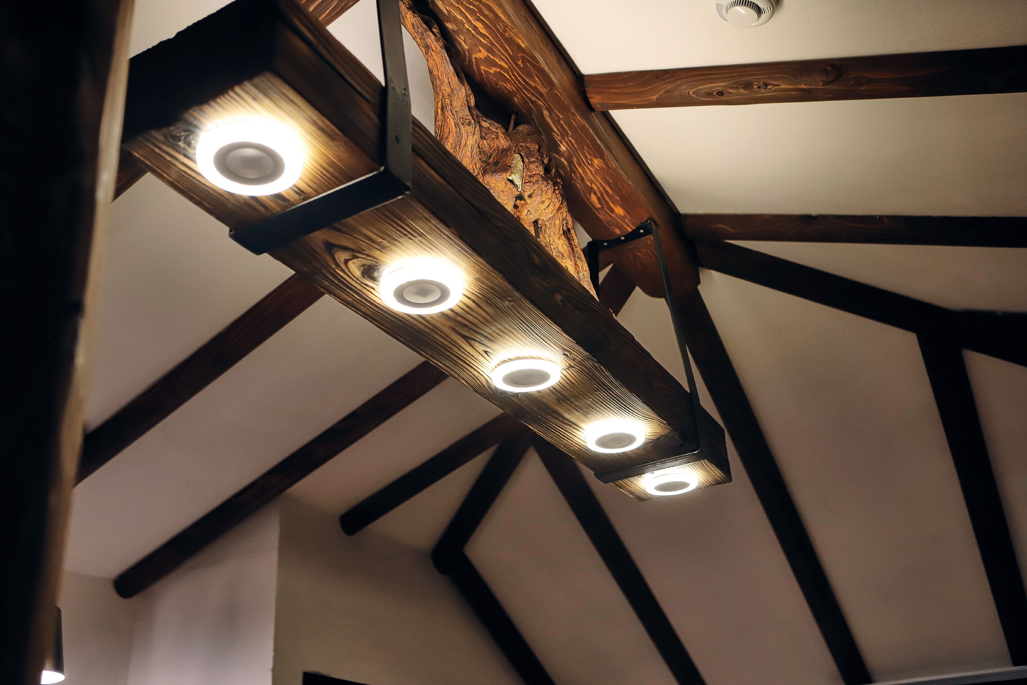 Teto com vigas de madeira aparentes e luminária moderna com quatro lâmpadas.